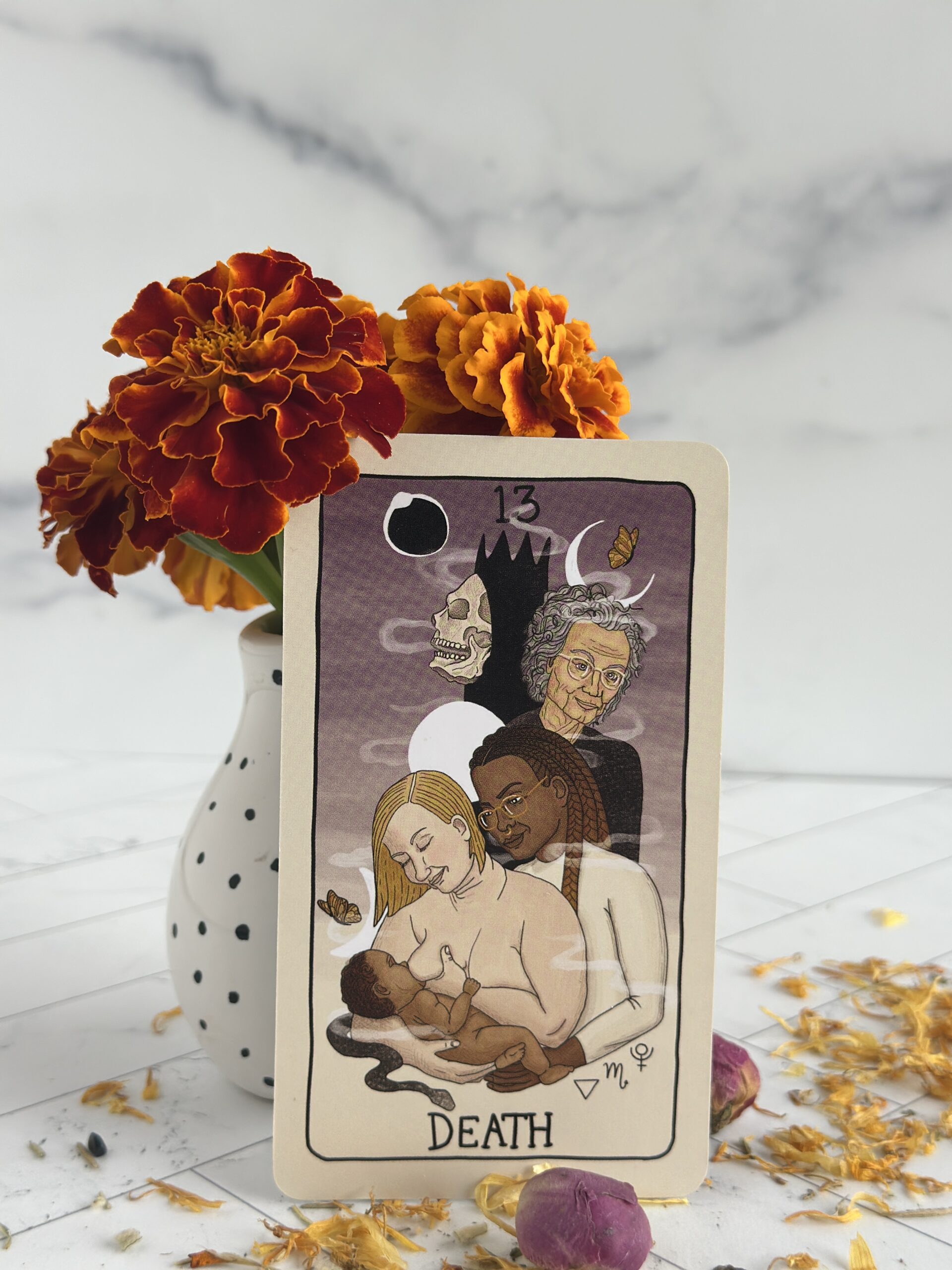 The Death tarot card by Charlie Claire Burgess, propped up on a vase of marigolds.